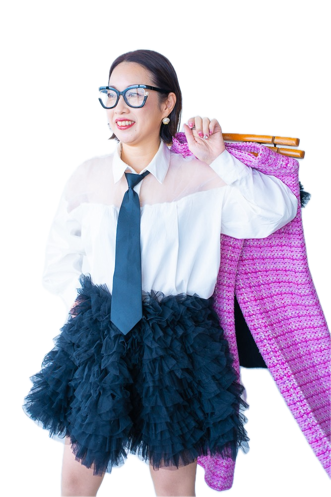 白いシャツに黒のネクタイ、黒のチュールスカートでピンクのツイードジャケットを肩にかけて笑う hime